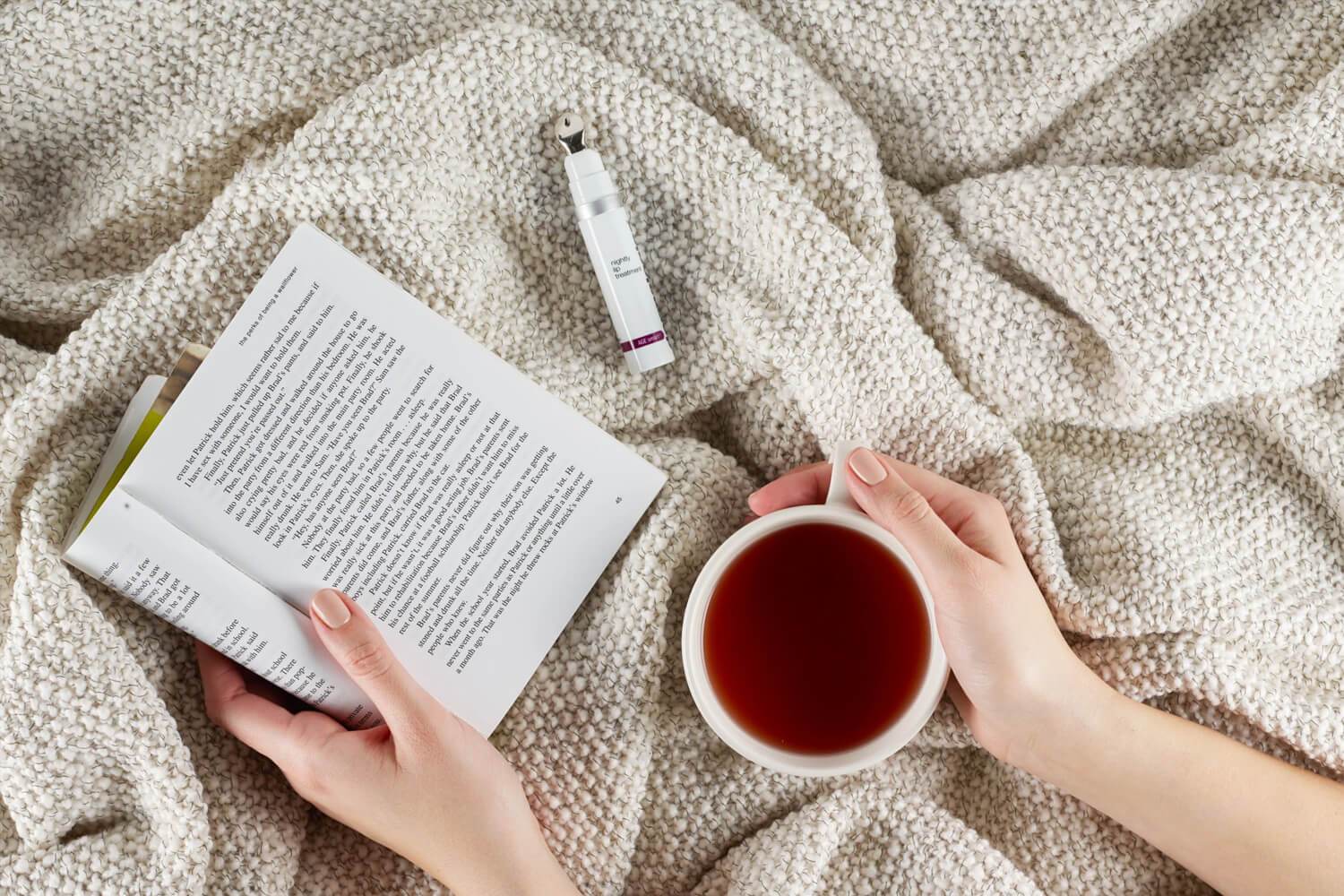 hands holding book and tea cup